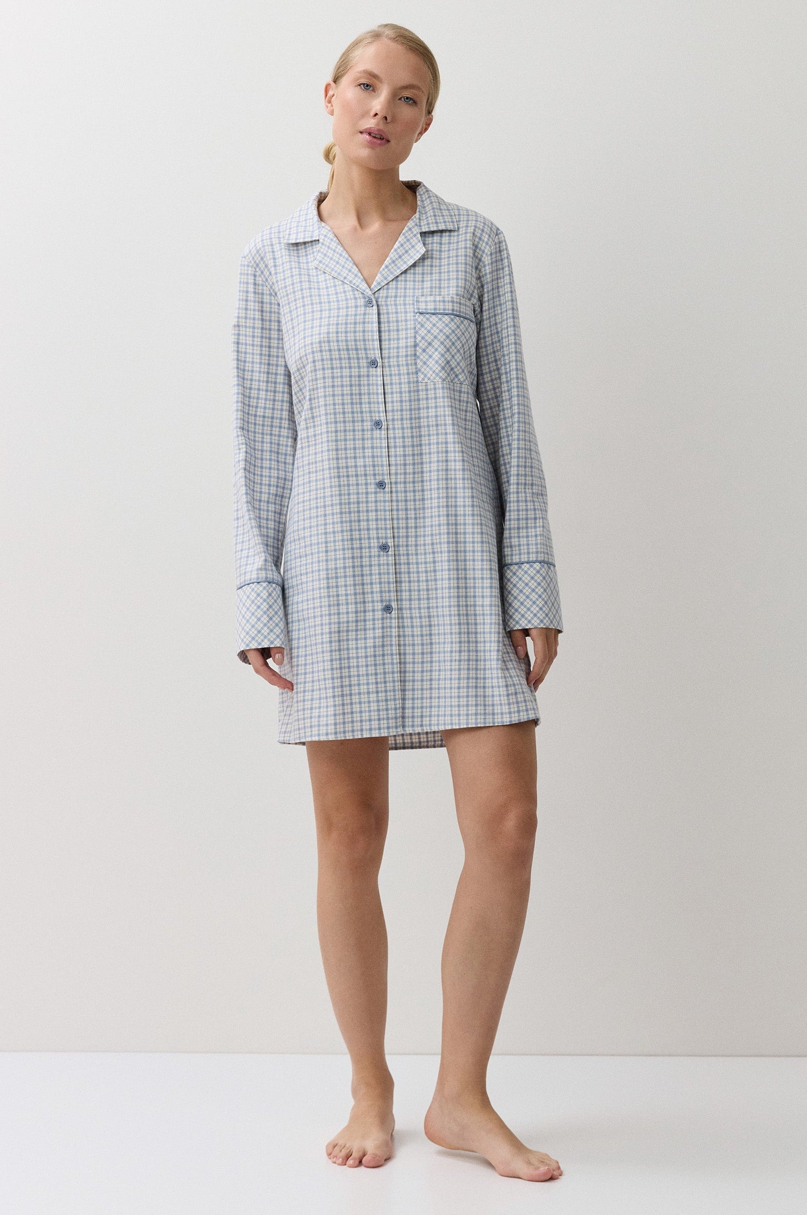 A woman modeling a light blue and white gingham check long-sleeve pajama shirt dress against a plain white studio background.