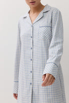 A woman wearing a light blue and white checkered long-sleeve button-up nightshirt, shown from the neck down against a plain light background.