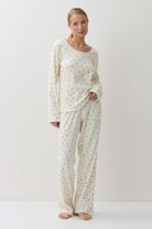 A woman modeling a two-piece long-sleeve pajama set with a small repeating floral pattern on an off-white base, standing against a plain white studio background.
