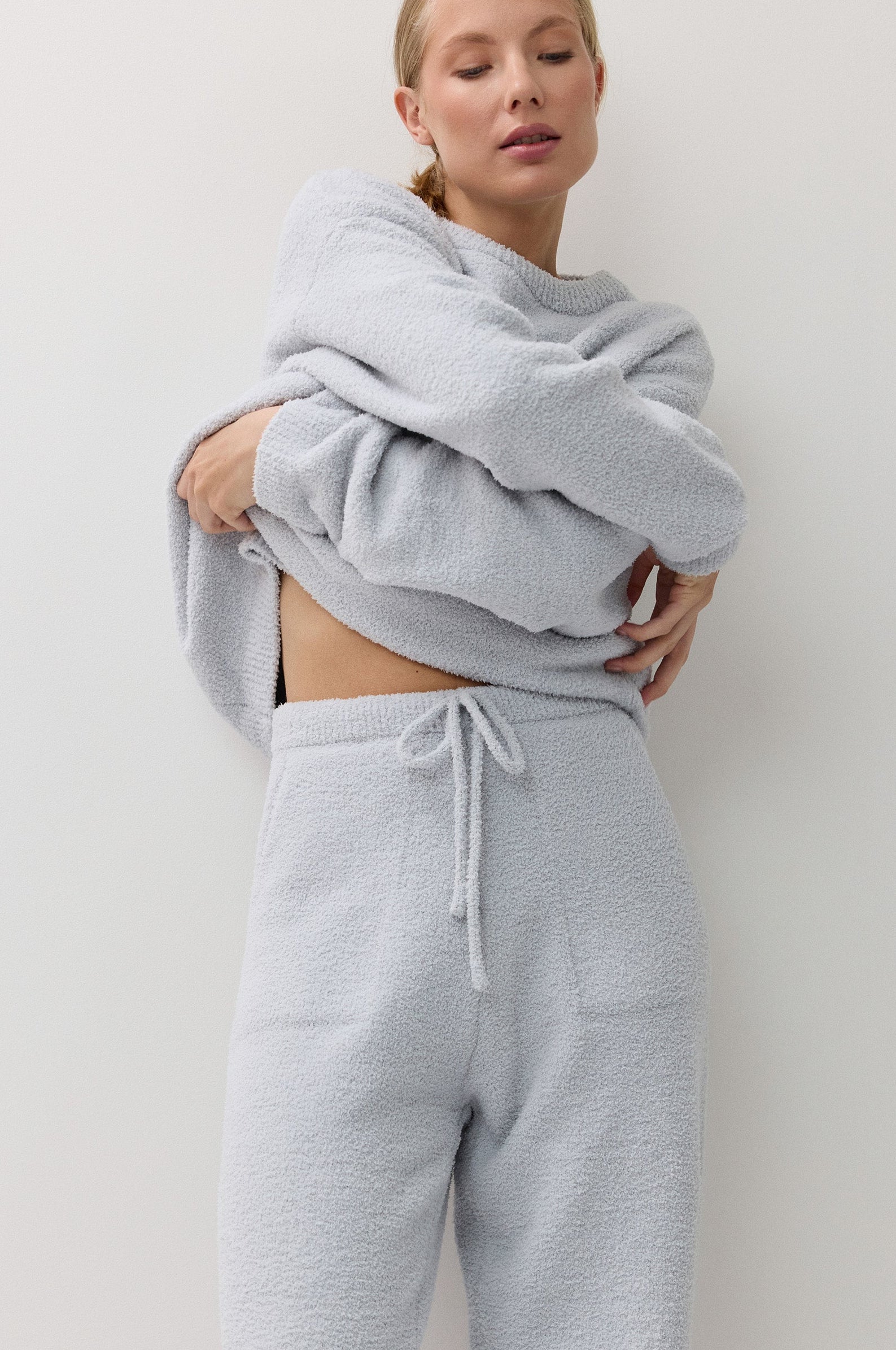 A woman modeling a light blue textured loungewear set consisting of a sweatshirt and matching drawstring sweatpants against a plain off-white background.