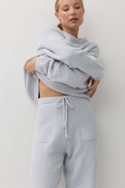 A woman modeling a light blue textured loungewear set consisting of a sweatshirt and matching drawstring sweatpants against a plain off-white background.