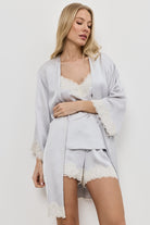 Woman wearing a light gray gown with lace trim over a matching pajama set on a white background