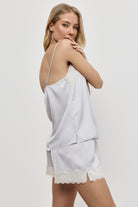 Woman wearing a light gray pajama set with lace trim on a white background