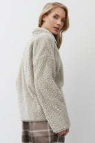 Woman wearing a textured beige sweater and plaid pants on a white background