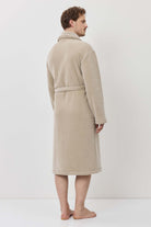 Person wearing a beige robe standing against a white background