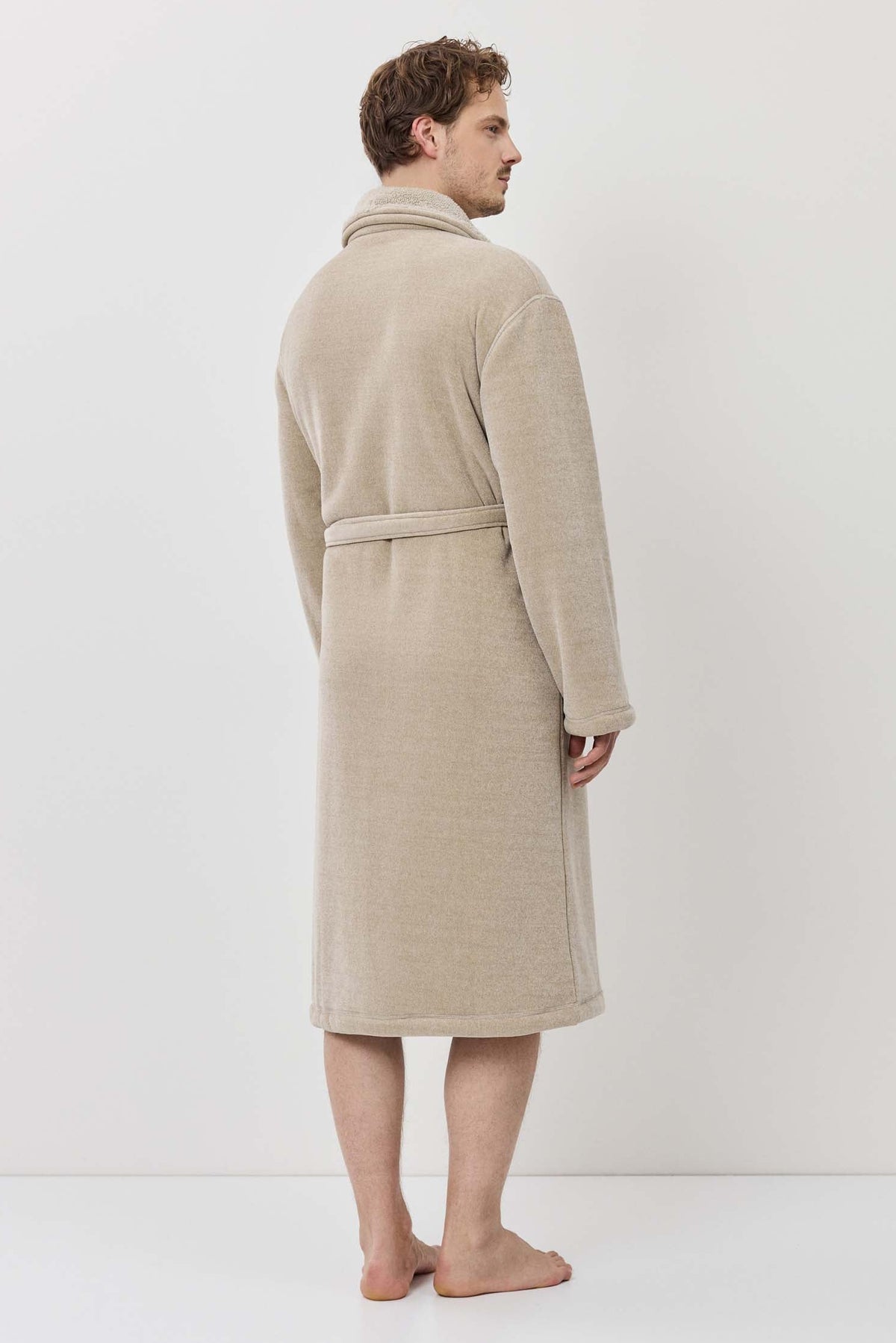Person wearing a beige robe standing against a white background