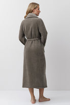 Woman wearing a brown bathrobe standing against a white background