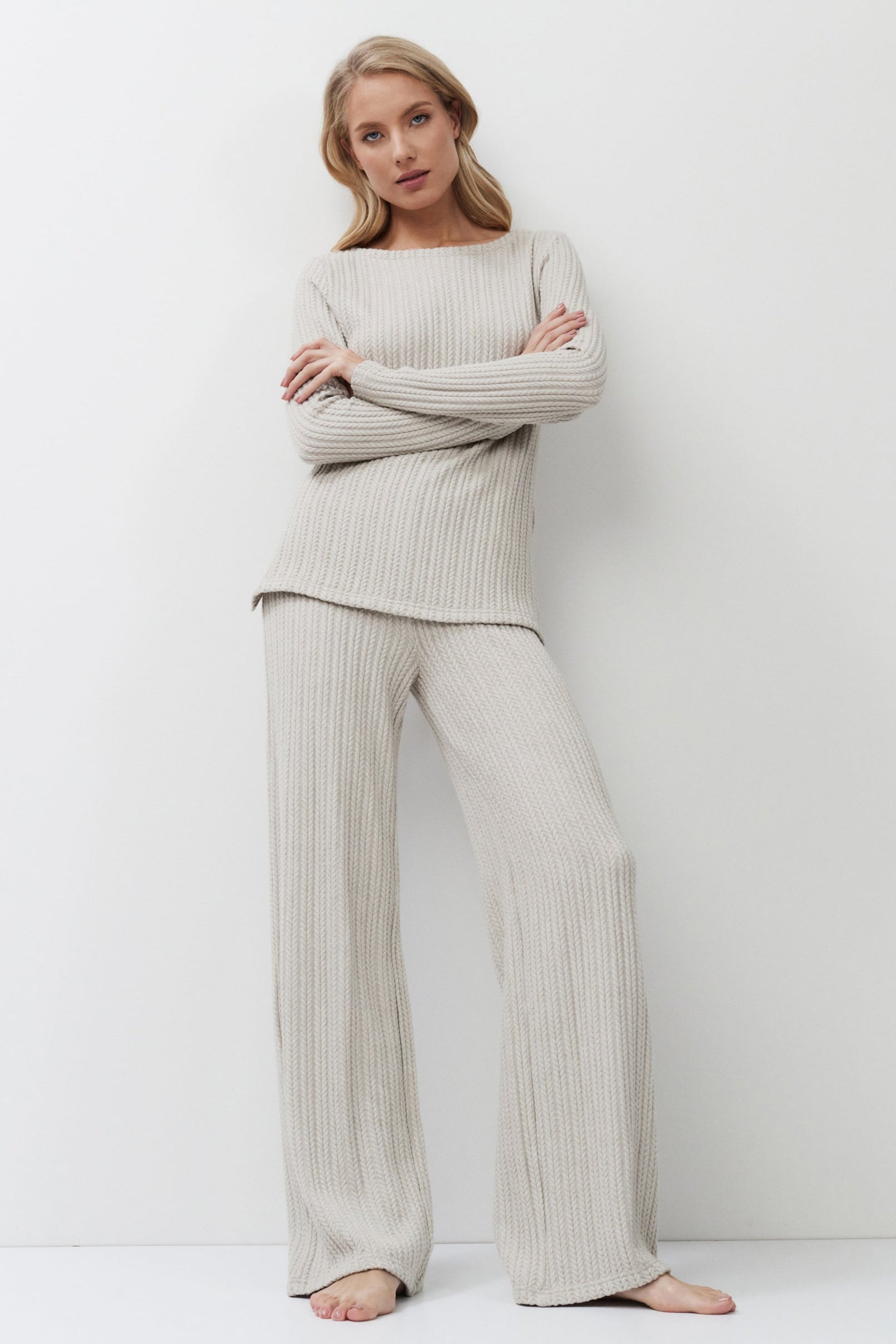 Woman wearing a beige ribbed sweater and pants against a white background