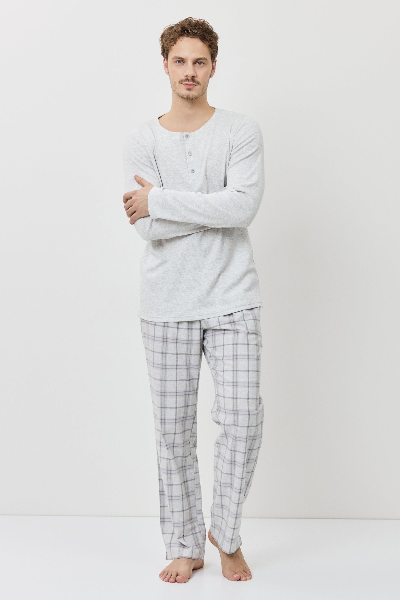Man wearing a light gray long-sleeve shirt and plaid pajama pants on a white background