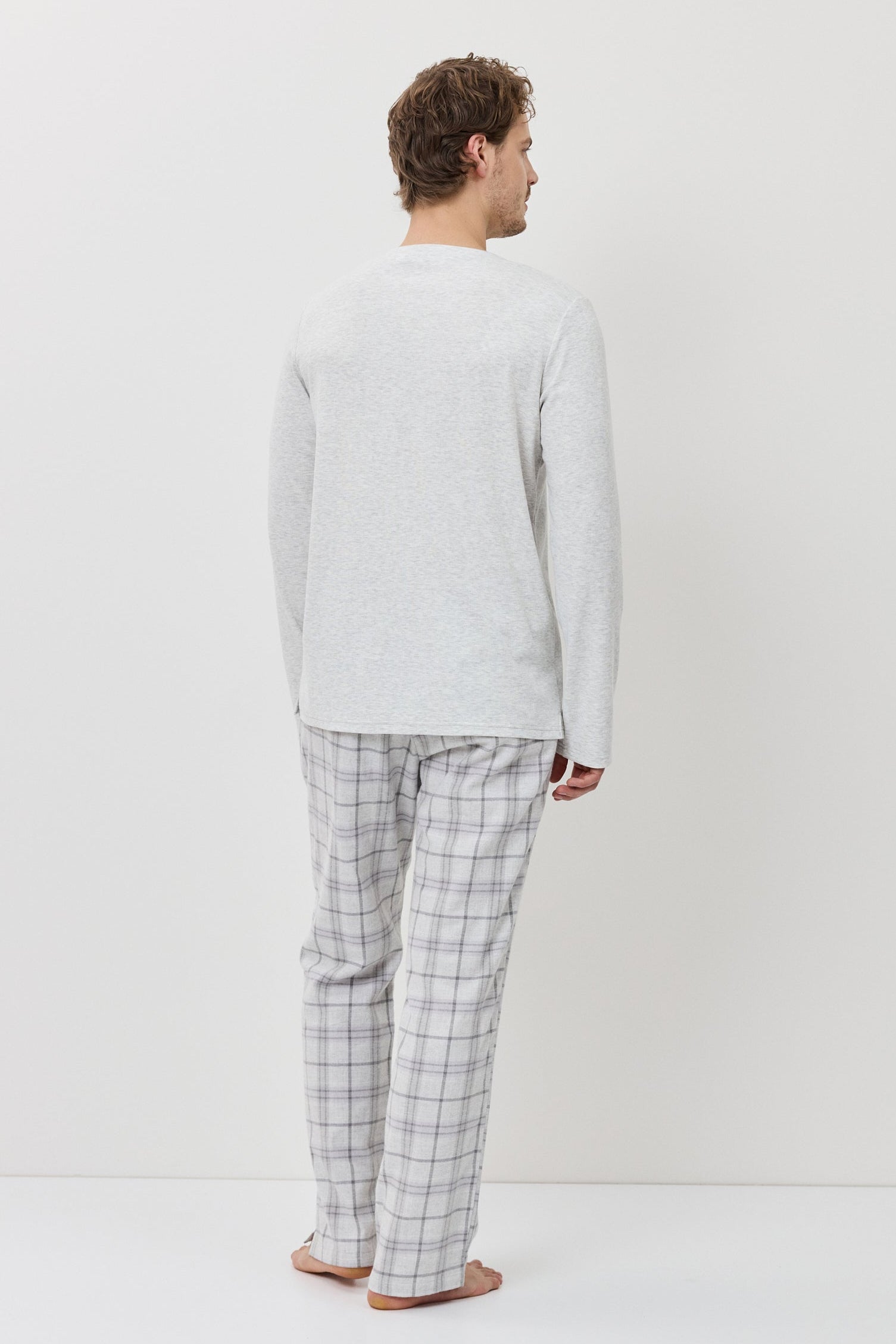 Man wearing a light gray sweater and checkered pants standing against a white background