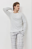 Man wearing a light gray long-sleeve shirt and plaid pants against a white background