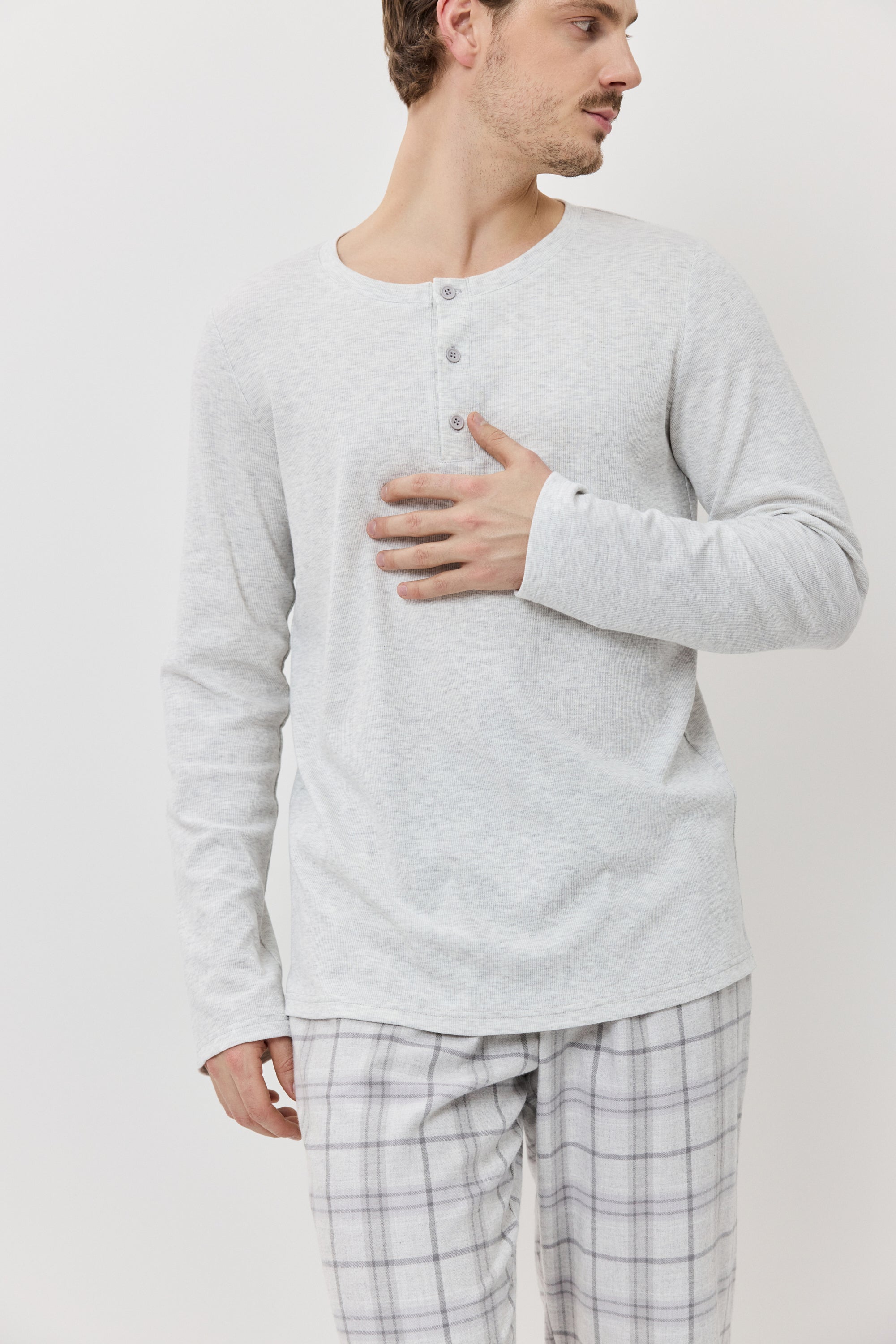 Man wearing a light gray long-sleeve shirt and plaid pajama pants on a plain background