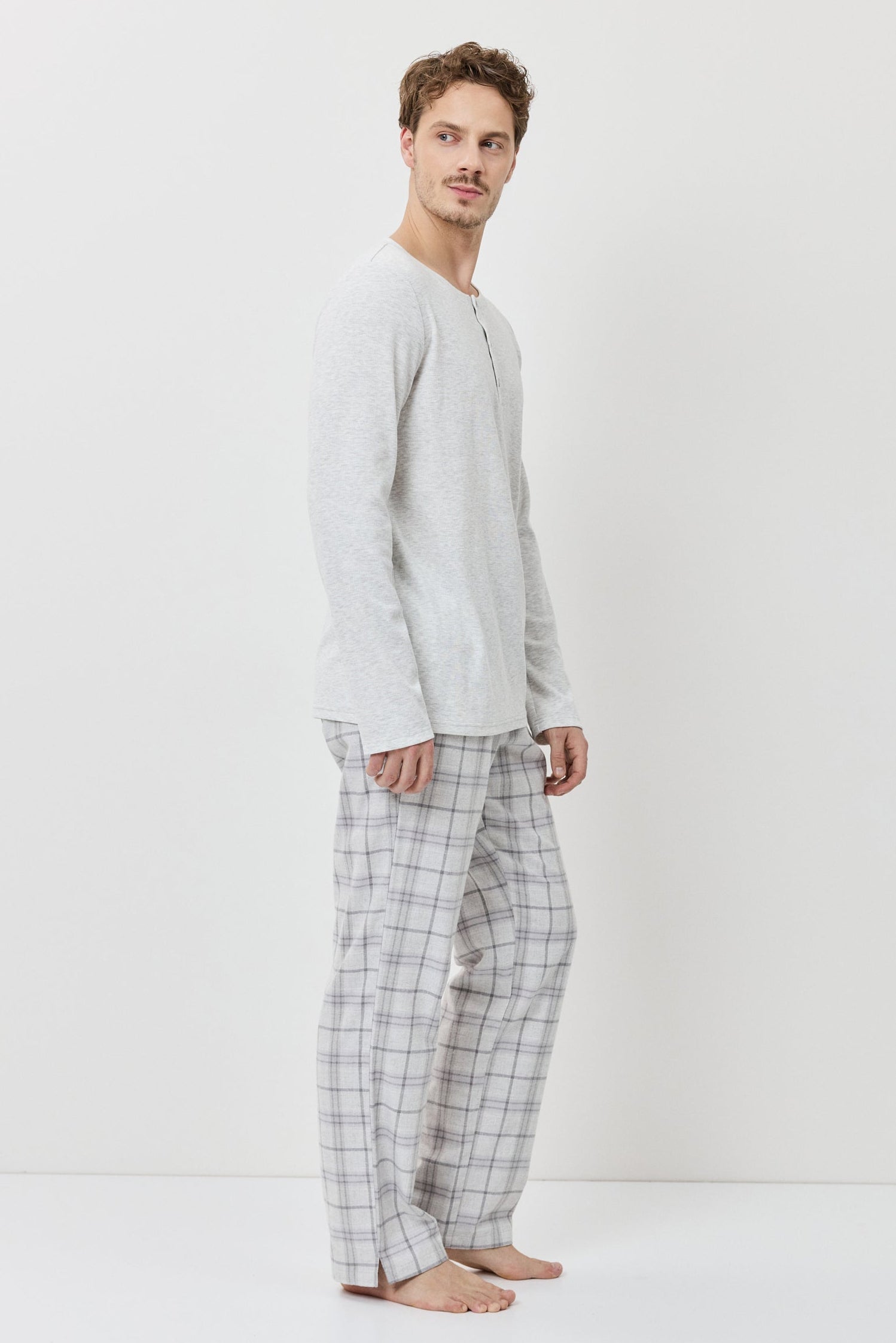 Man wearing a light gray long-sleeve shirt and checkered pants on a white background