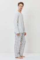 Man wearing a light gray long-sleeve shirt and checkered pants on a white background