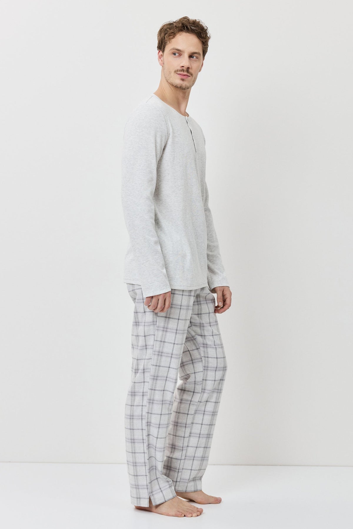 Man wearing a light gray long-sleeve shirt and checkered pants on a white background