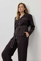 Woman wearing a black pajama set with white piping against a light gray background