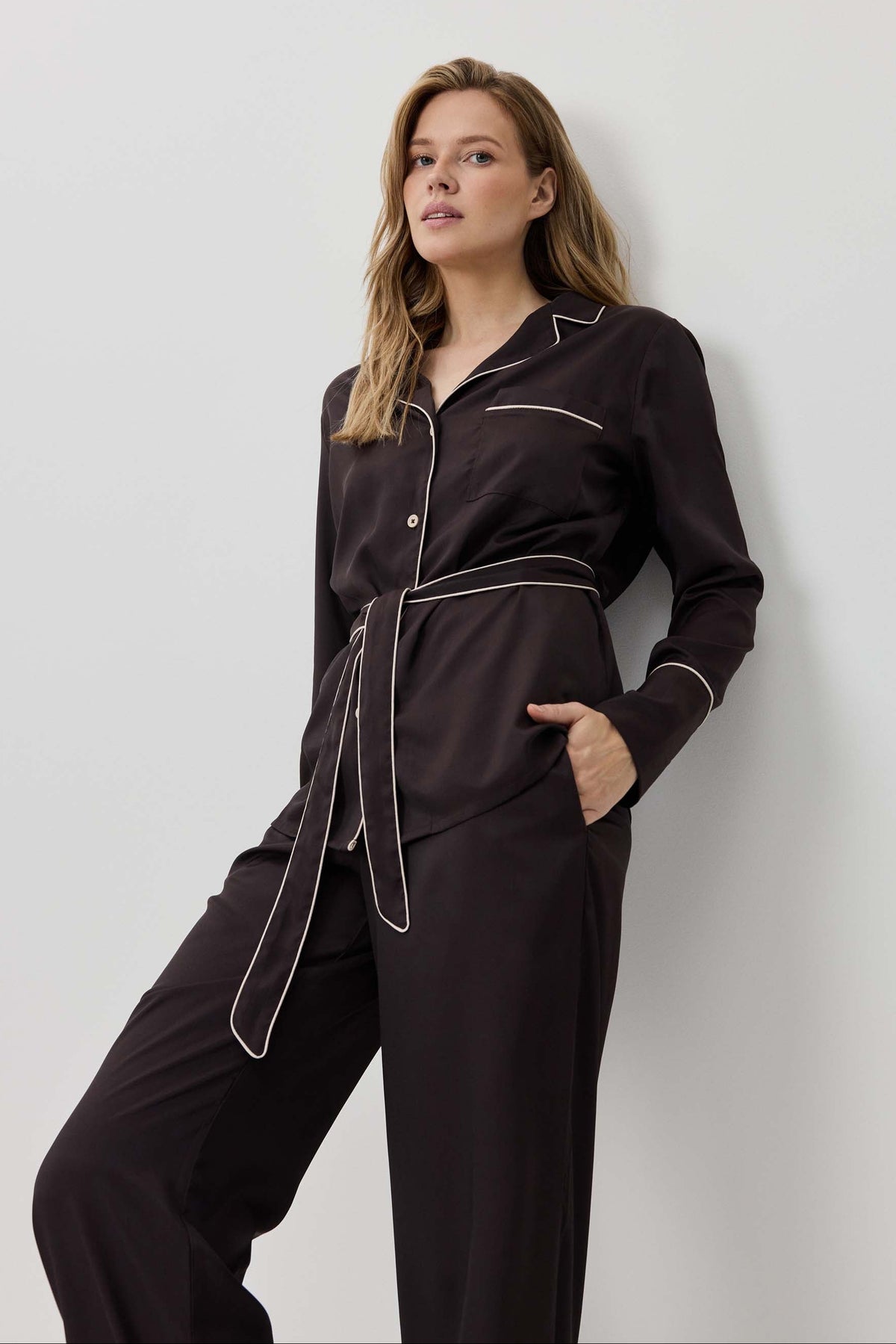 Woman wearing a black pajama set with white piping against a light gray background