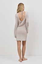 Woman wearing a beige dress with a cut-out back design on a white background