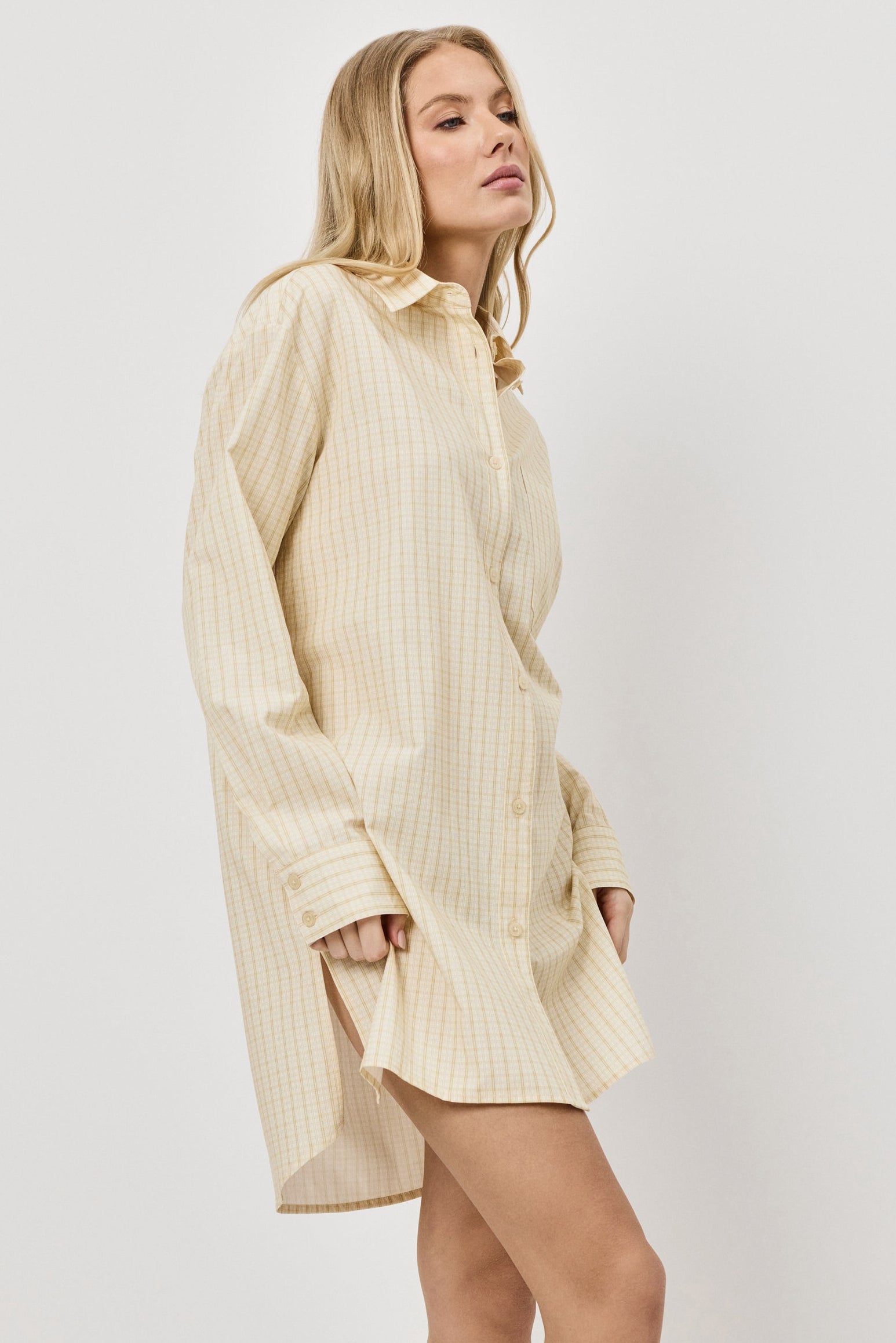 Woman wearing a long yellow shirt nightdress against a white background