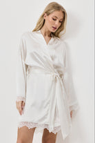 Woman wearing a white gown with lace hem on a plain background