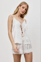 Woman wearing a white lace-trimmed pajama set against a plain background