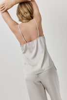 Woman wearing a light gray satin pajama set with thin straps on a plain background