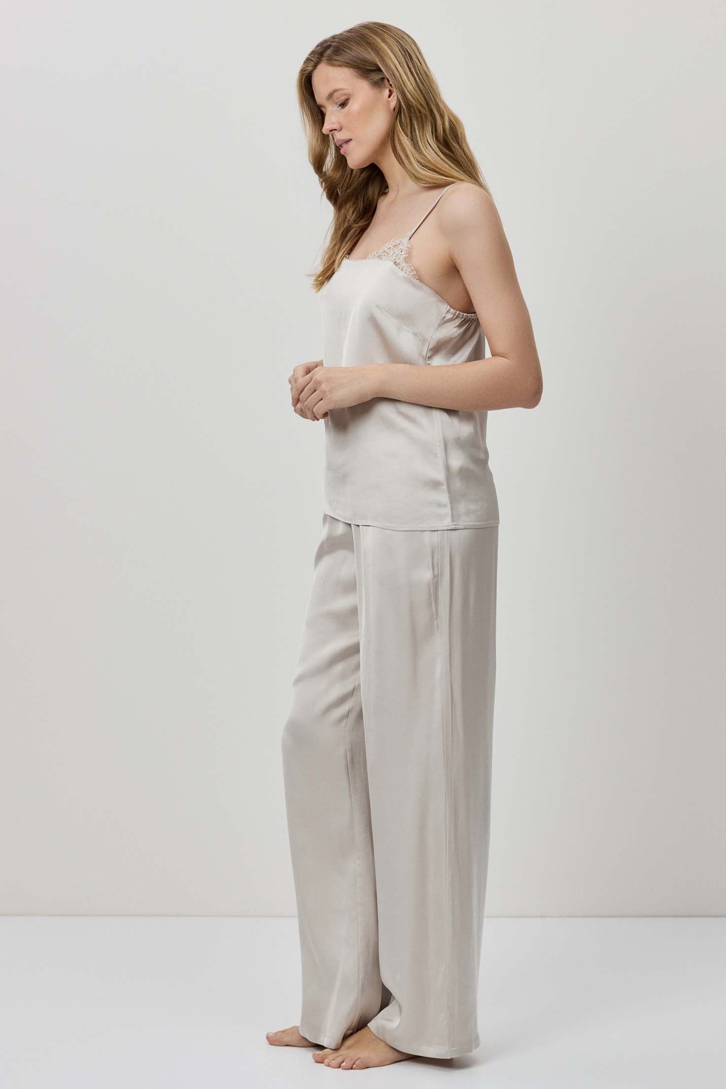 Woman wearing a light-colored satin top and wide-leg pants on a white background