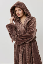 Woman wearing a brown plush robe against a plain background