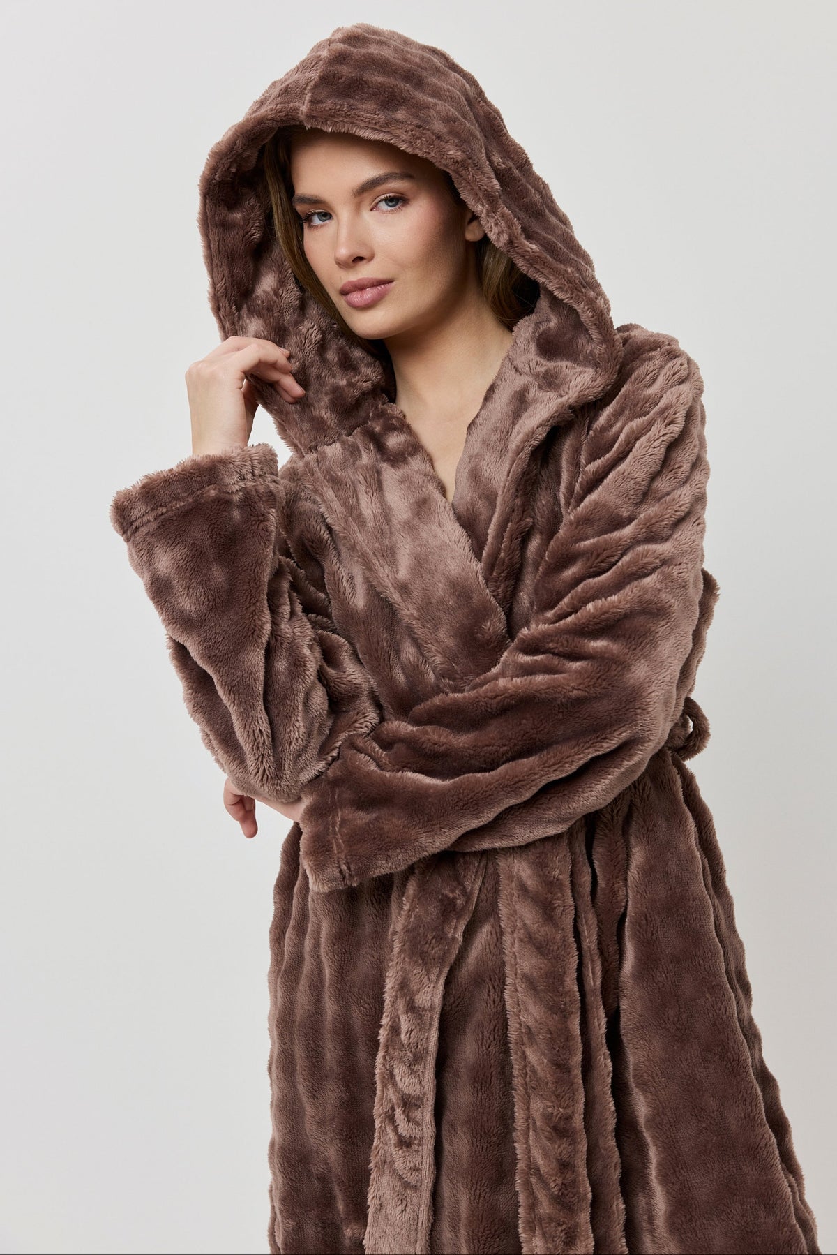 Woman wearing a brown plush robe against a plain background