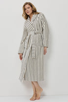 A woman modeling a long-sleeved, knee-length striped bathrobe with a matching tie belt, standing against a plain white studio background.