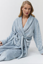 Woman wearing a light blue bathrobe against a white background