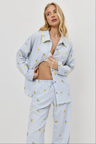Woman wearing a light blue pajama set with lemon embroideries on a plain background
