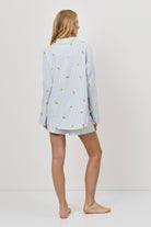 Woman wearing a light blue pajama set with lemon embroideries on a white background