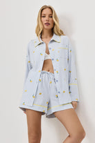 Woman wearing a light blue pajama set with lemon emroideries on a white background