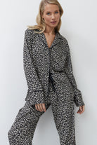 Woman wearing a leopard print pajama set with pants against a white background