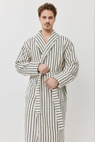 A man wearing a long-sleeved striped bathrobe with black and white vertical stripes.