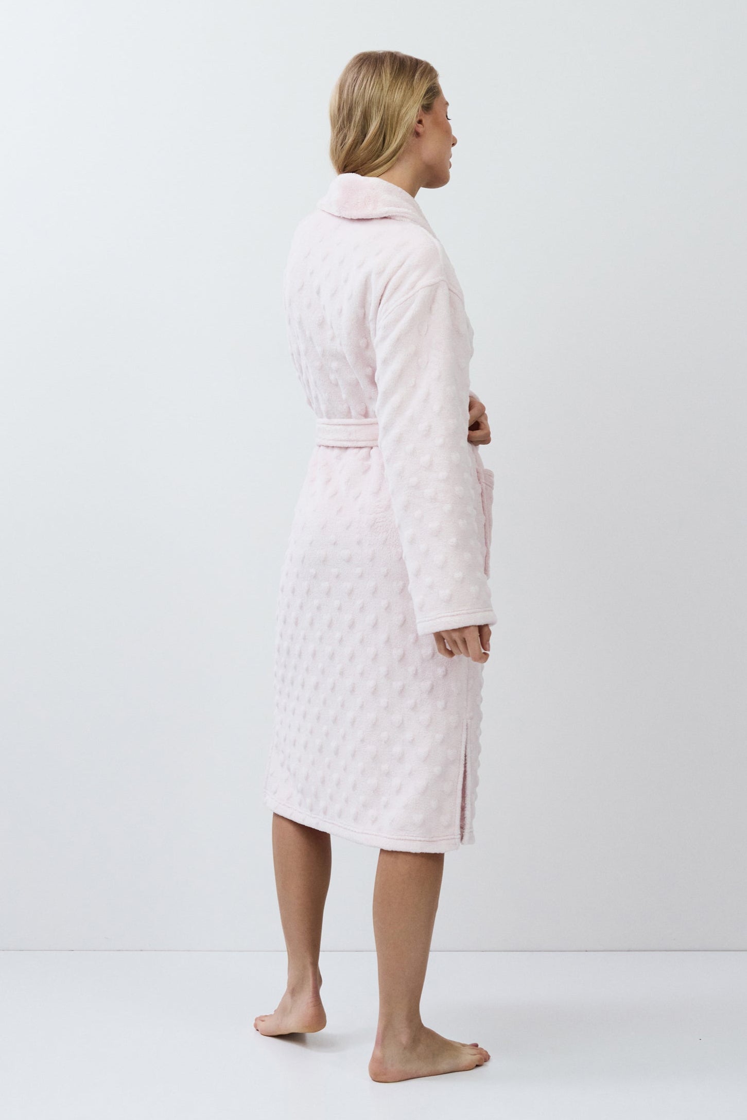 Person wearing a light pink quilted bathrobe on a white background