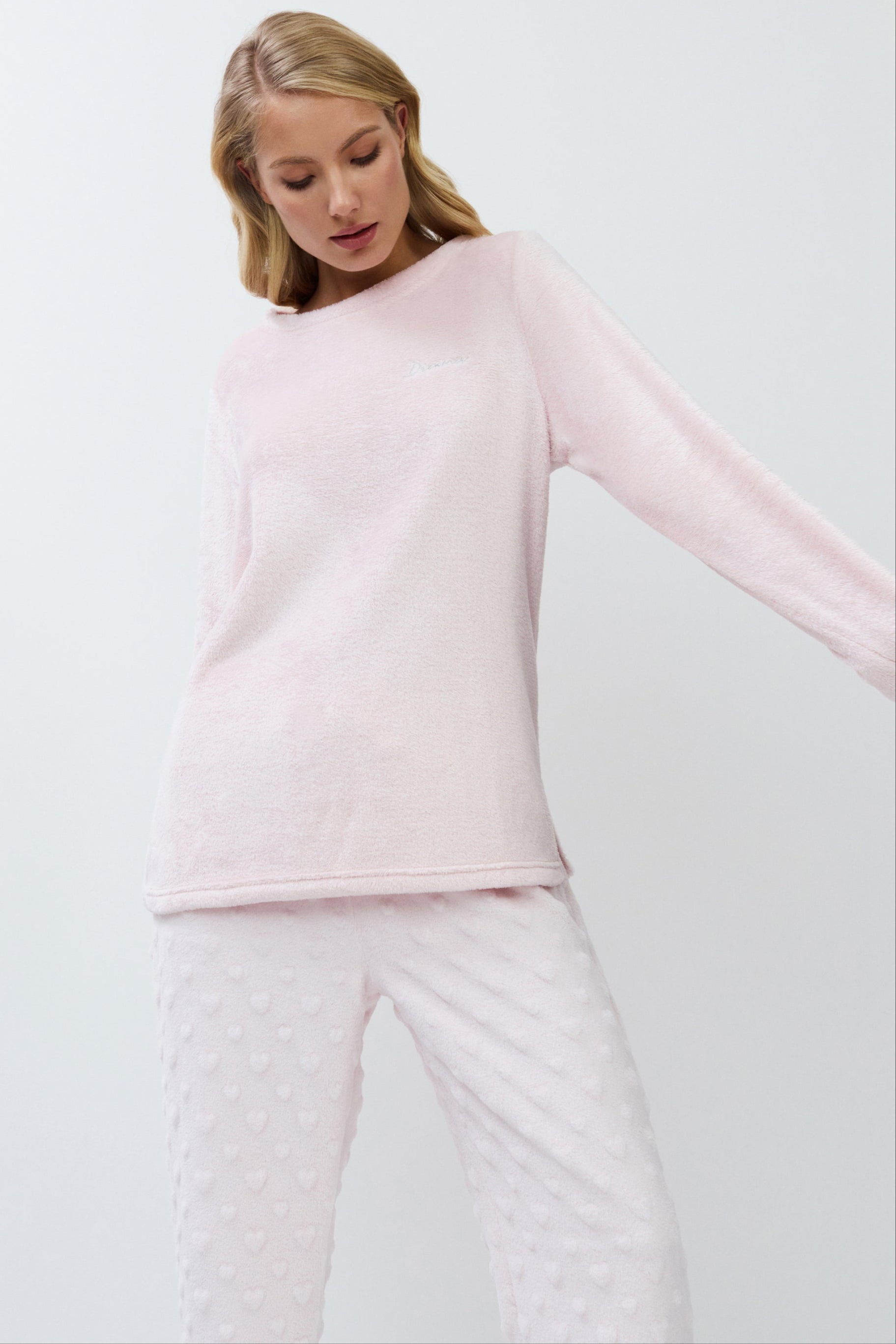 Woman wearing a light pink sweater and white pants on a white background