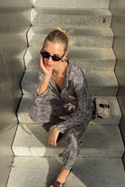 Woman sitting on a set of stairs wearing sunglasses and a patterned pajama set.