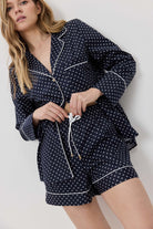 Woman wearing a navy blue polka dot pajama set against a white background