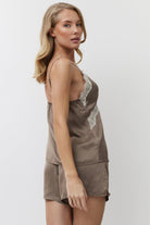 Woman wearing a brown satin pajama set with lace details on a white background