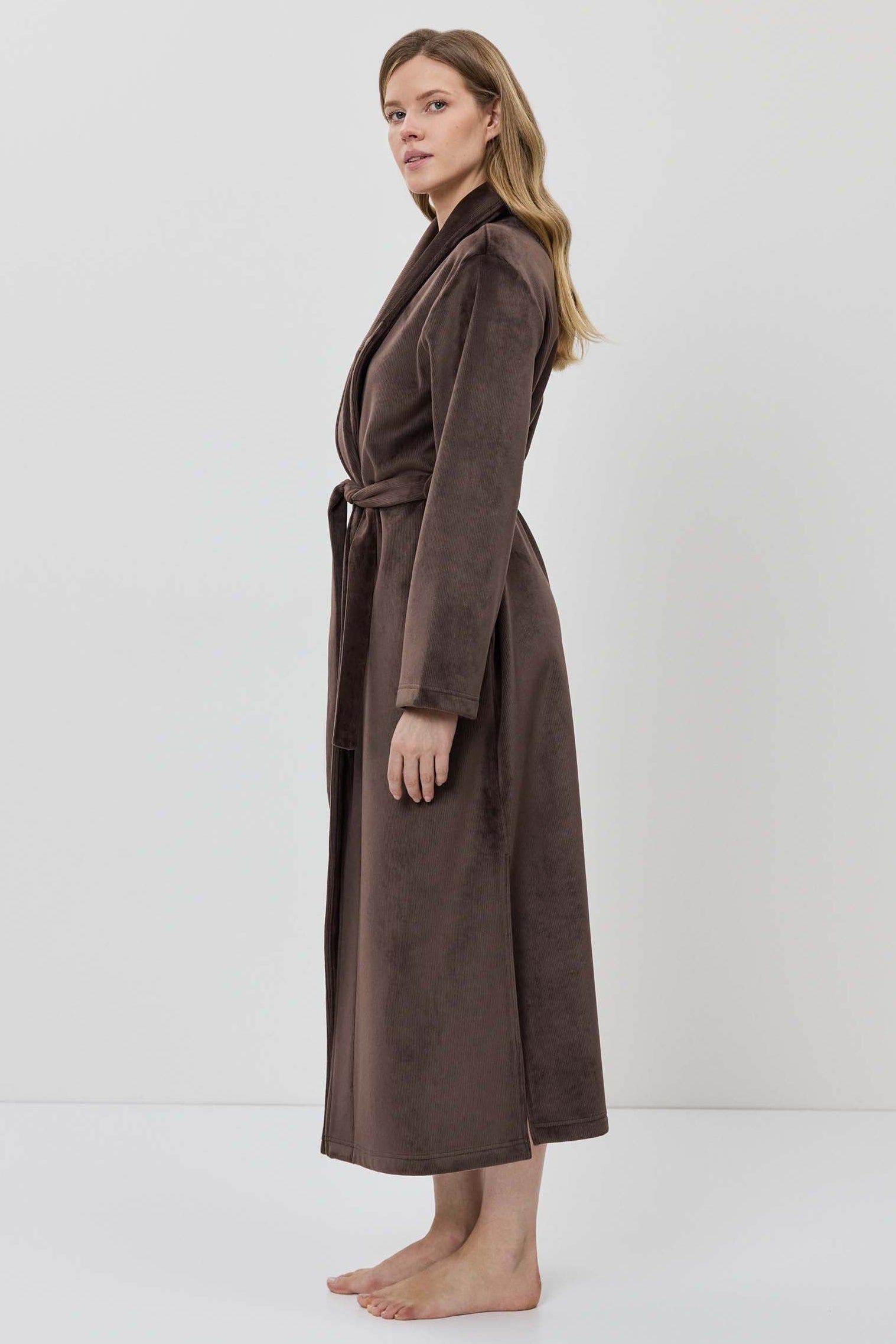 A woman wearing a long brown plush bathrobe with a tie belt.