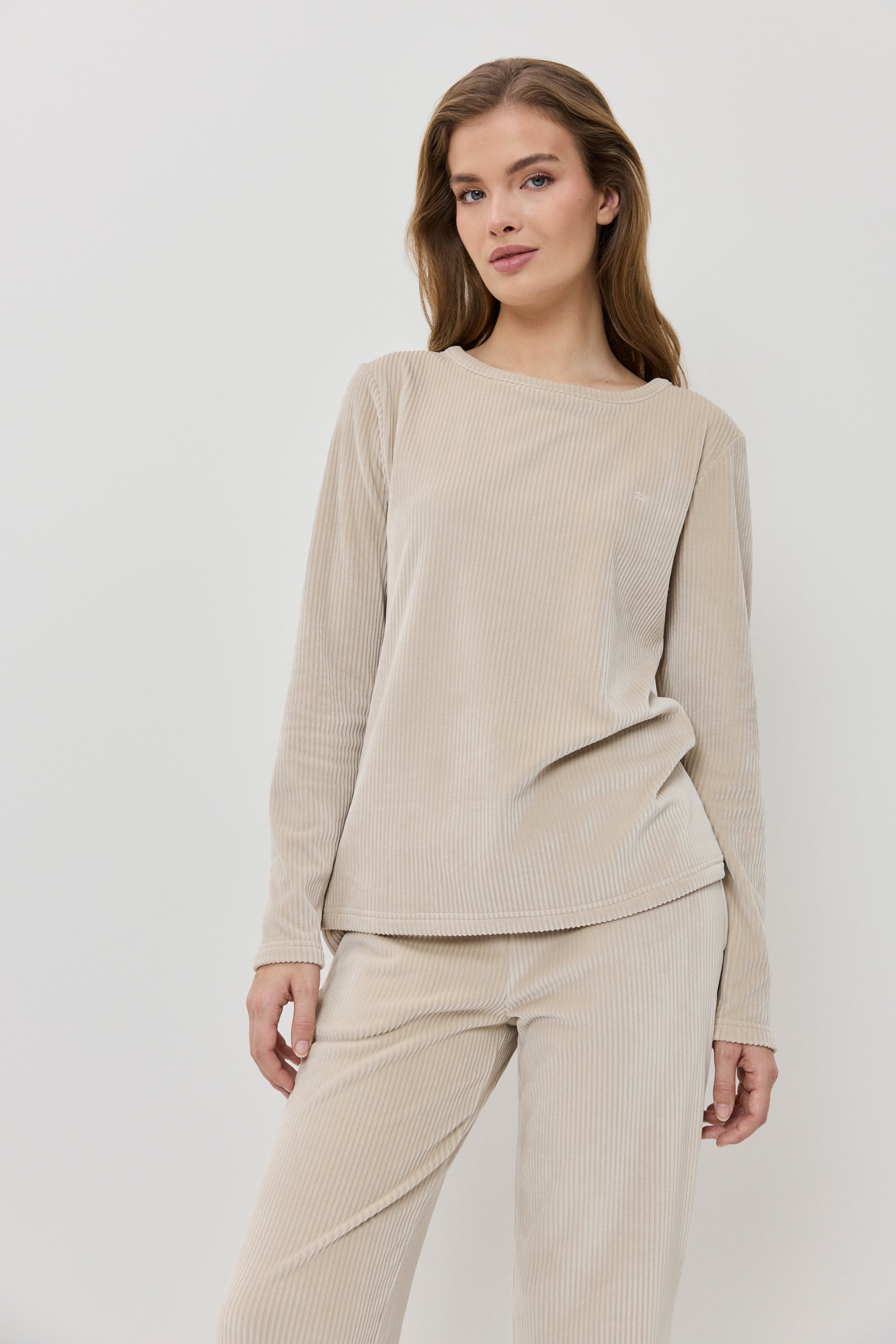 Woman wearing a beige ribbed sweater and pants on a white background