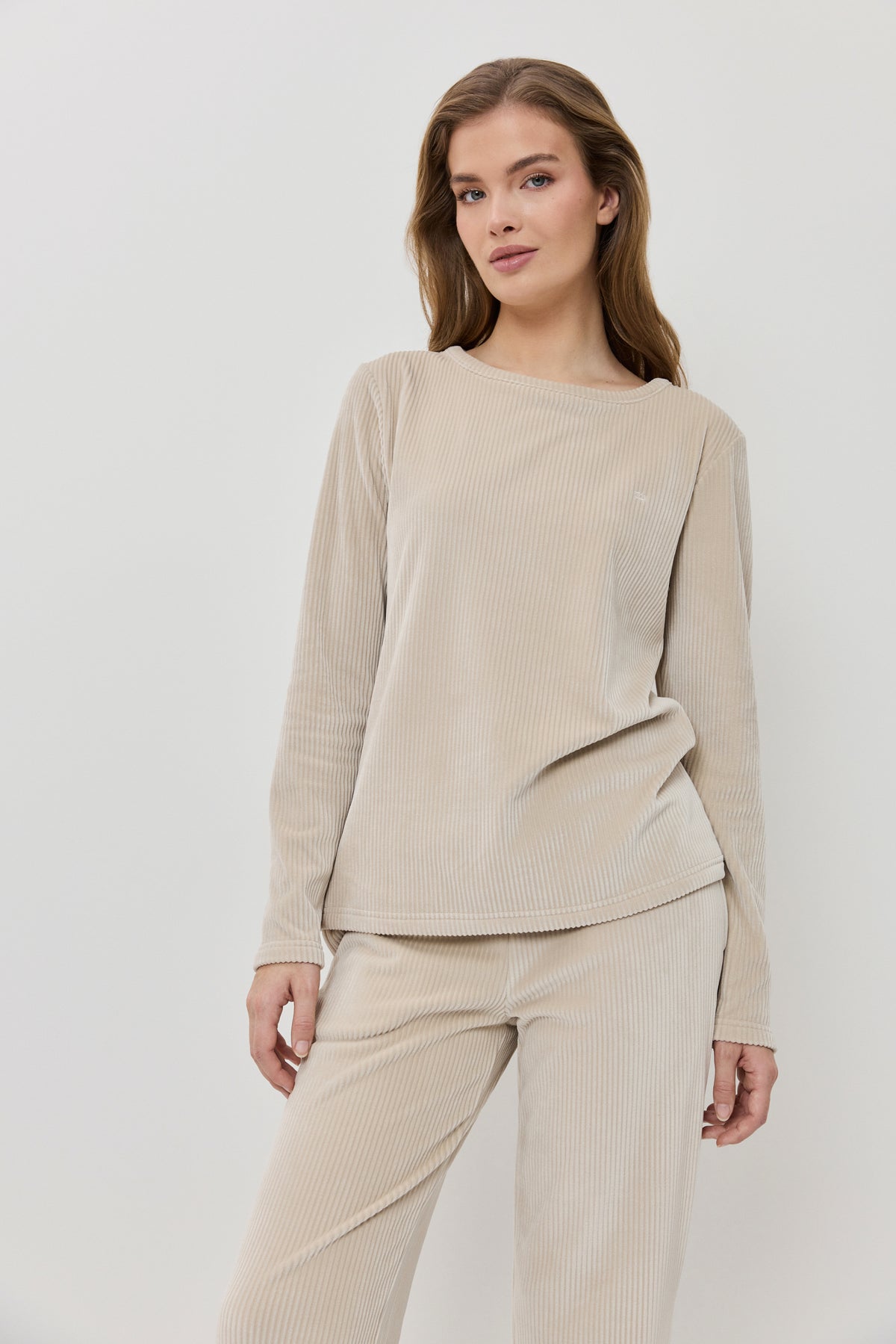 Woman wearing a beige ribbed sweater and pants on a white background