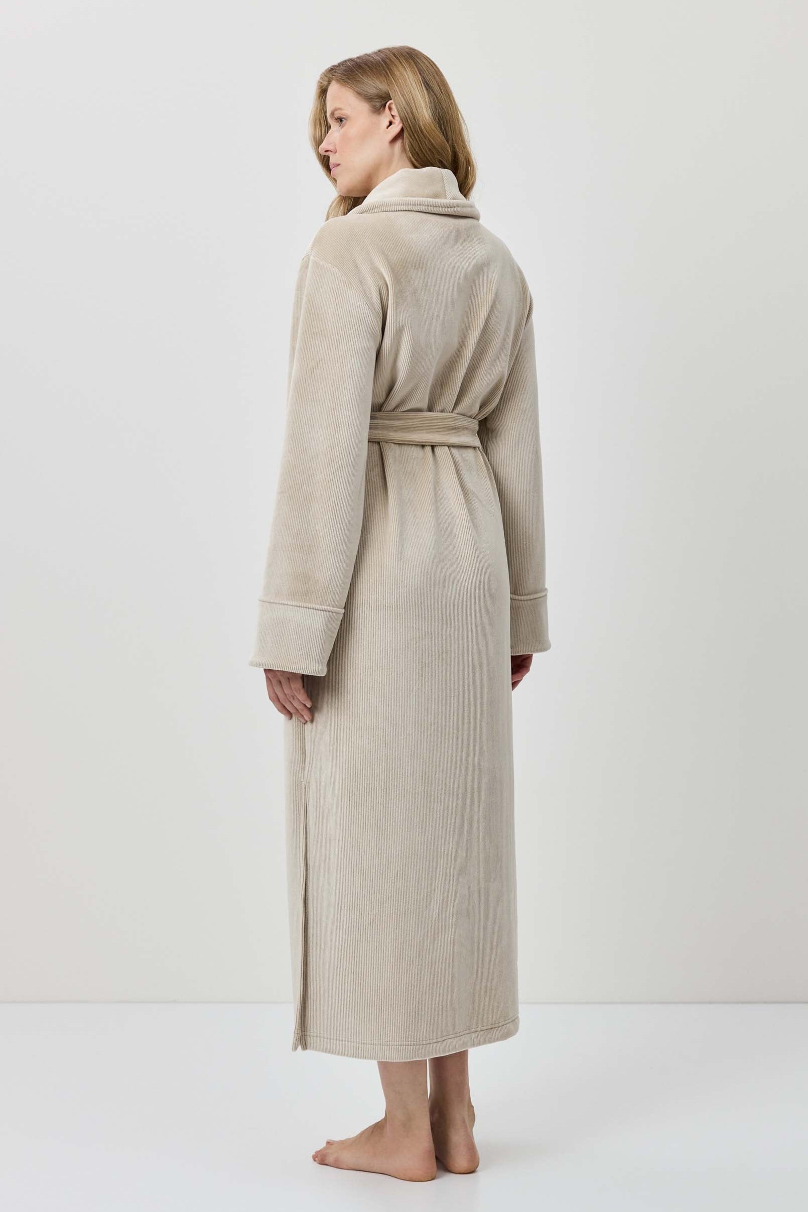 Woman wearing a beige robe standing against a white background
