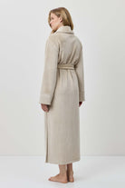 Woman wearing a beige robe standing against a white background