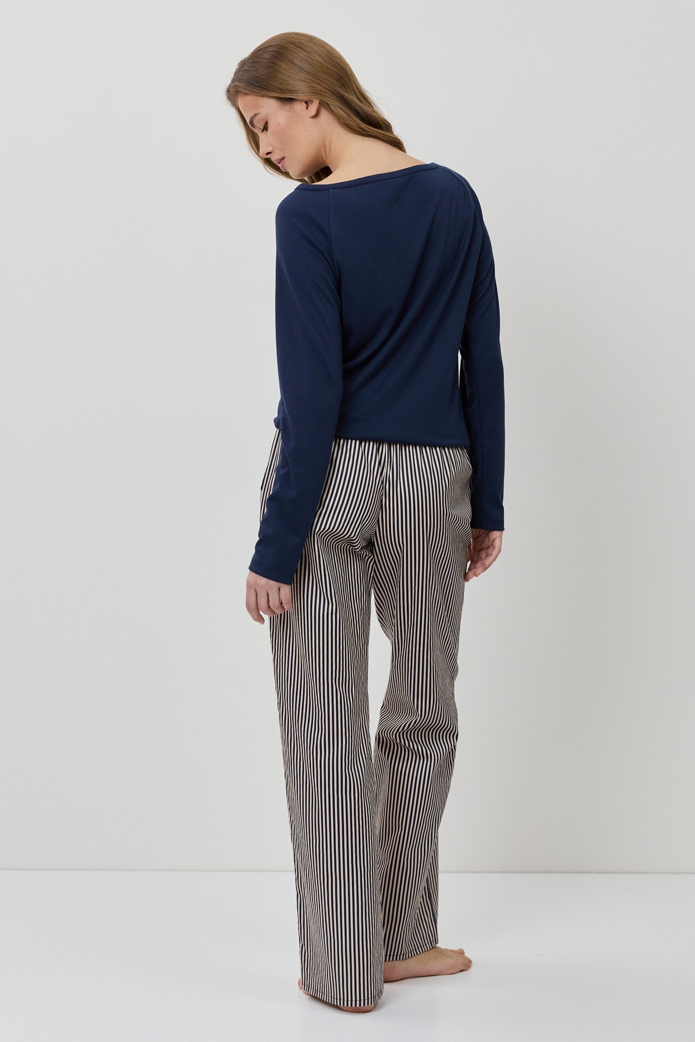 Woman wearing a navy sweater and gray striped pants on a white background