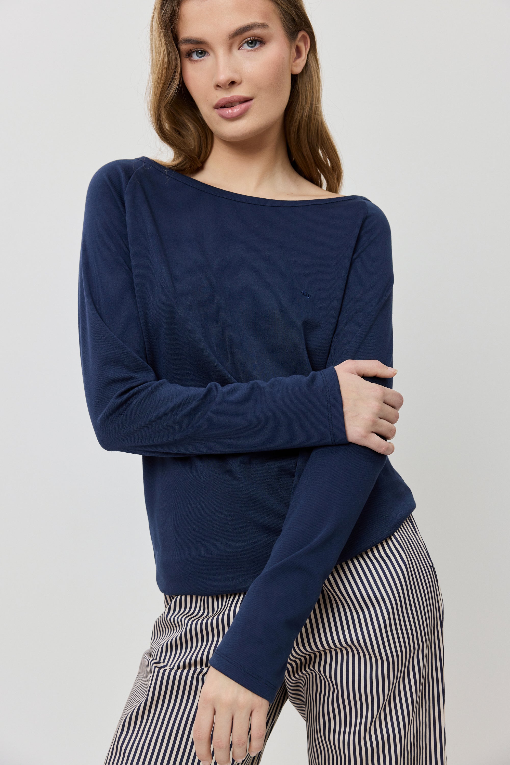 Woman wearing a navy blue sweater and striped pants on a light gray background