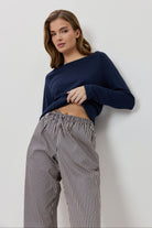 Woman wearing a navy blue sweater and striped pants against a white background