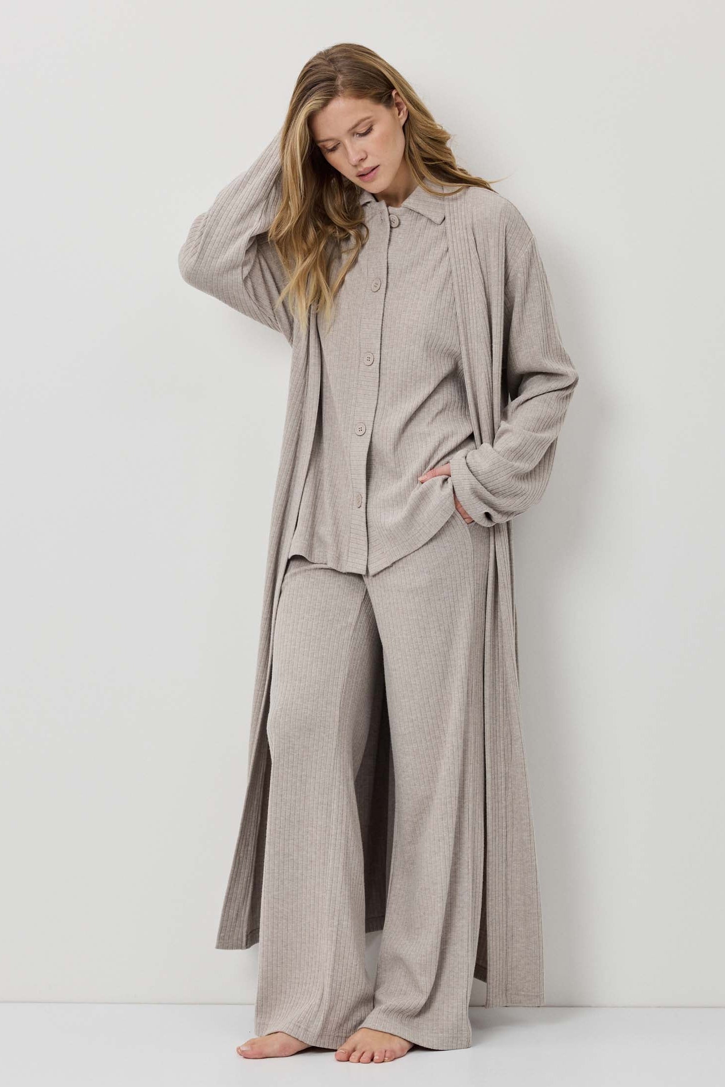 Woman wearing a beige long-sleeve shirt and wide-leg pants against a white background